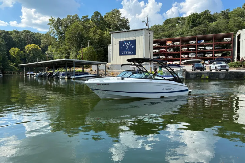 Slide: The Image of 2025 Regal LS2 boat cruising near a marina with docked boats and lush greenery. - 10