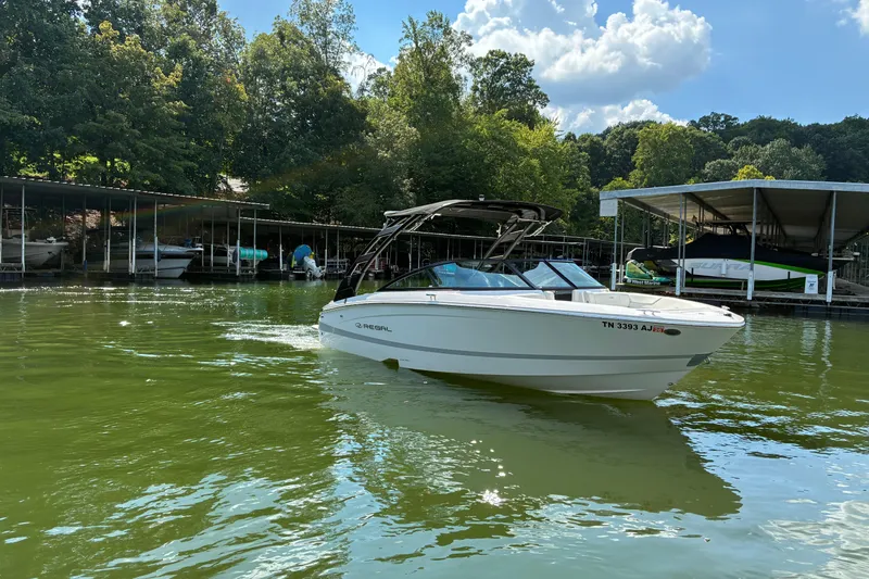 Slide: The Image of 2025 Regal LS2 boat on a serene lake near a marina, surrounded by lush trees. - 5