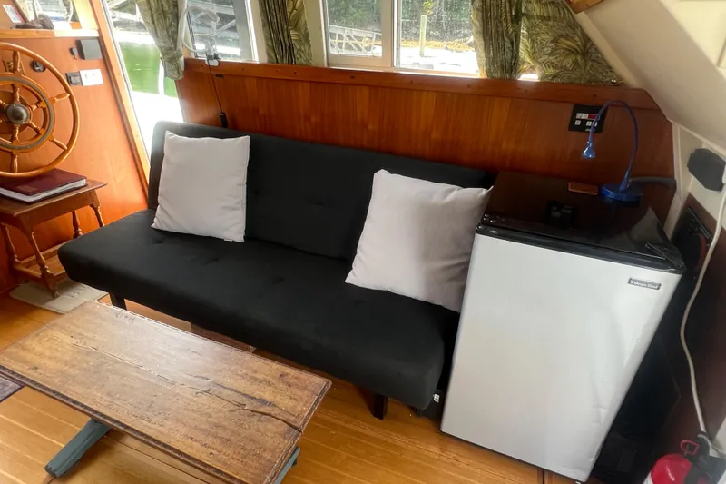Slide: The Image of Interior of 2001 Mainship 390 Trawler with sofa, mini fridge, and wooden steering wheel. - 2