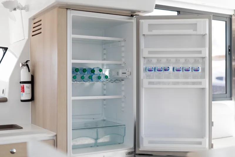 Slide: The Image of Open fridge on Bali 4.0 yacht, stocked with bottled water, next to a fire extinguisher. - 13