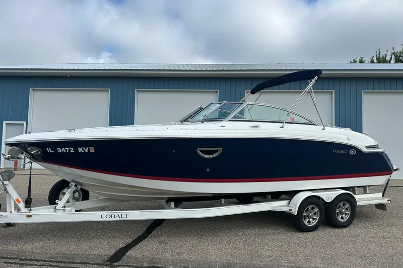 Slide: The Image of 2010 Cobalt 276 boat on trailer, parked outside blue building under cloudy sky. - 14