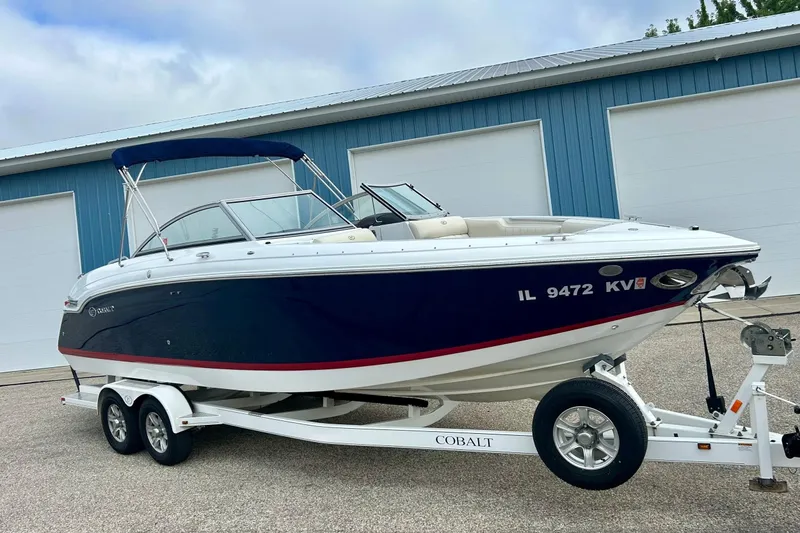 Slide: The Image of 2010 Cobalt 276 boat on trailer, parked near blue garage doors. - 2