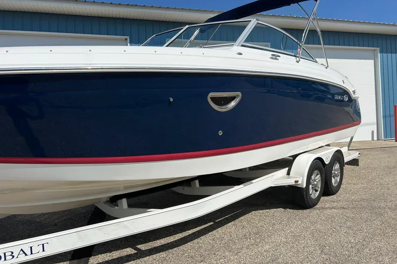 Slide: The Image of 2010 Cobalt 276 boat on trailer, blue and white exterior, parked near a blue building. - 38