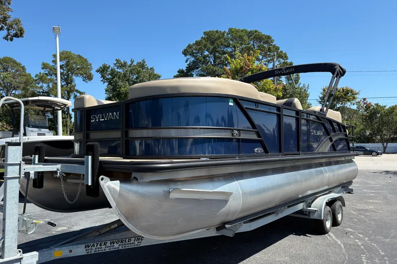 The Image of 2024 Sylvan L3 CLZ pontoon boat on trailer, parked outdoors under clear sky. - 0