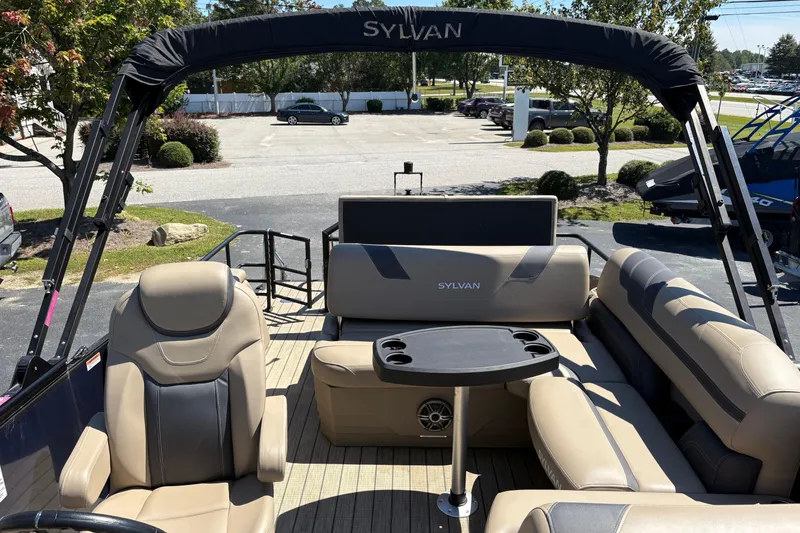 Slide: The Image of 2024 Sylvan L3 CLZ pontoon boat interior with seating and table, parked outdoors. - 17
