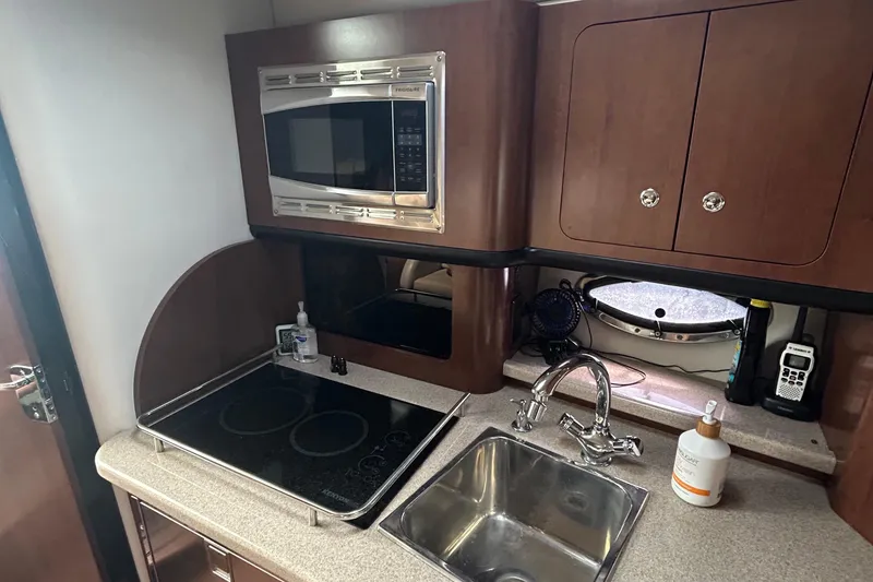 Slide: The Image of 2015 Crownline 350 SY yacht kitchen with microwave, stove, sink, and storage cabinets. - 31
