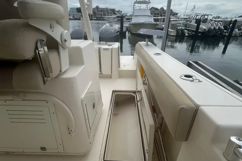 Slide: The Image of 2016 Cobia 296 Center Console boat interior at marina, featuring seating and storage compartments. - 23