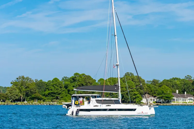 Slide: The Image of 2024 St Francis 460 catamaran sailing on a serene lake with lush greenery. - 169
