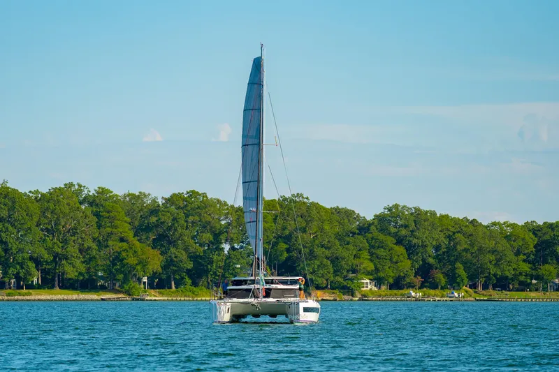 Slide: The Image of 2024 St Francis 460 catamaran sailing on a serene lake with lush green shoreline. - 172