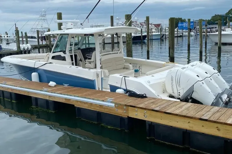 Slide: The Image of 2019 Boston Whaler 380 Outrage docked, featuring triple outboard engines, in a marina setting. - 2