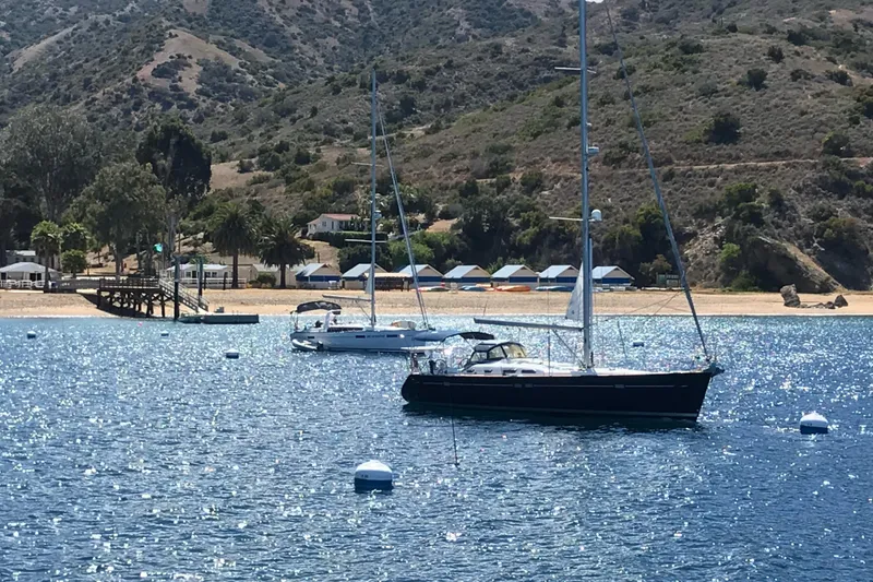 Slide: The Image of Sailboats anchored near a scenic coastline, featuring a 2003 Beneteau Oceanis Clipper 473. - 6
