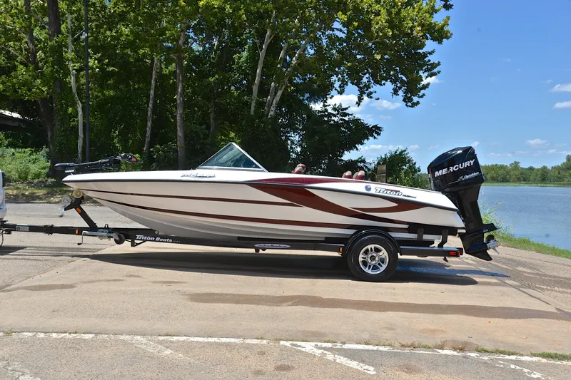 Slide: The Image of 2012 Triton 190 boat on trailer by a lake, featuring a Mercury outboard motor. - 11