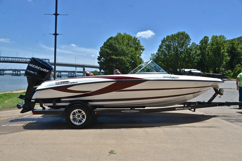 Slide: The Image of 2012 Triton 190 boat on trailer by river, clear sky, and trees in background. - 15