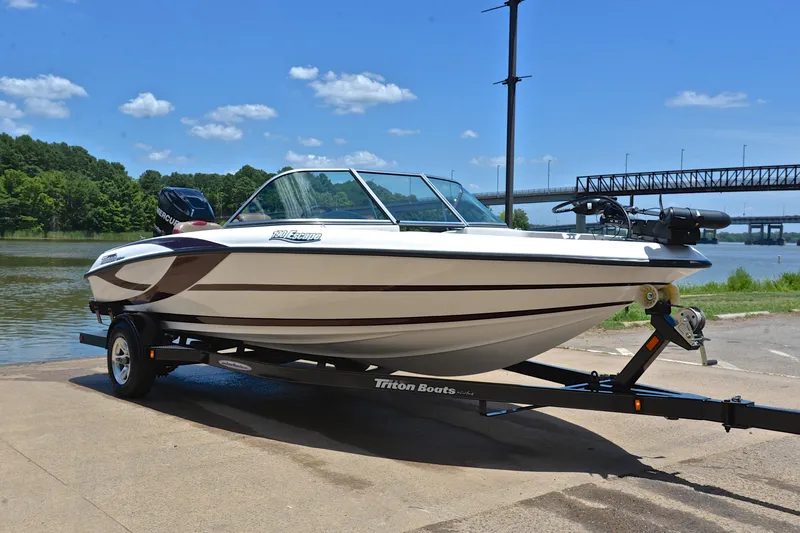 Slide: The Image of 2012 Triton 190 boat on trailer by river, clear sky, bridge in background. - 16