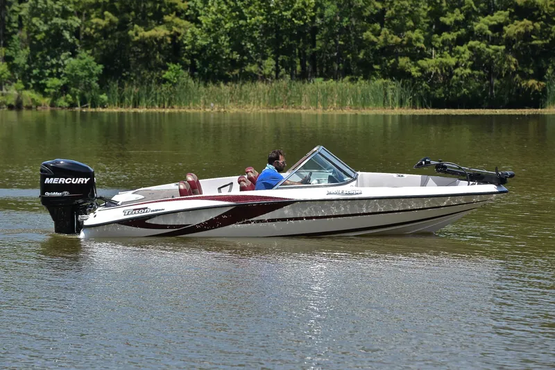 Slide: The Image of 2012 Triton 190 boat cruising on a calm lake with lush greenery. - 7