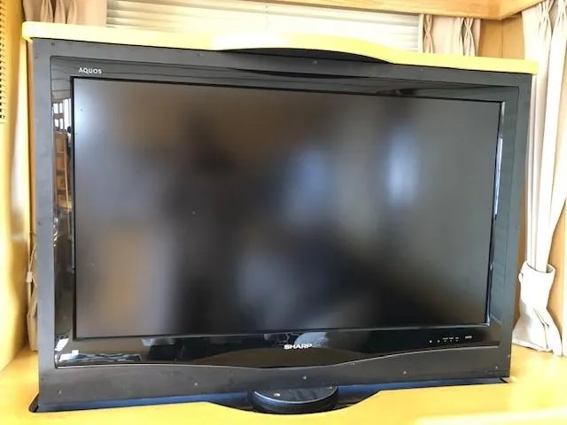 Slide: The Image of Sharp Aquos flat-screen TV on a wooden stand, surrounded by curtains. - 18