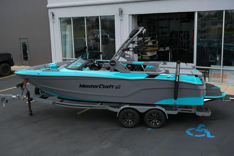 Slide: The Image of 2026 MasterCraft XT23 boat in gray and turquoise, parked on a trailer outside a showroom. - 3