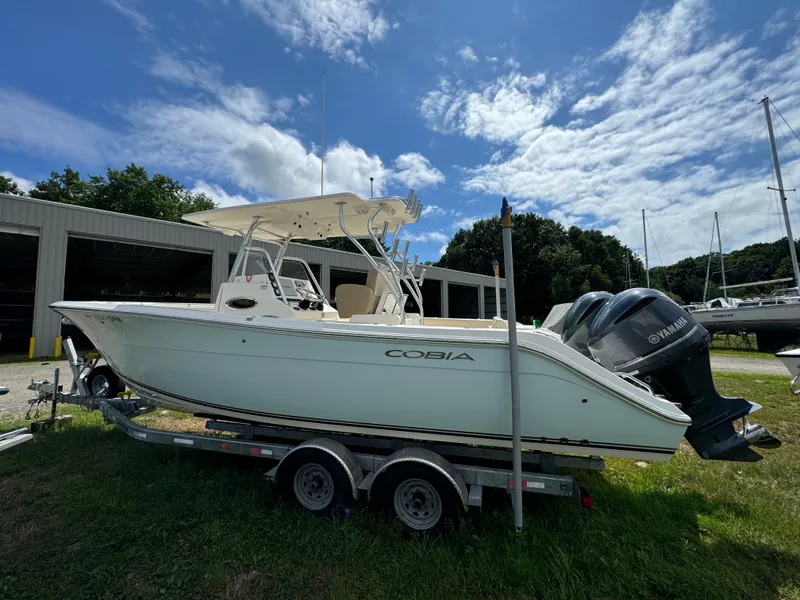Slide: The Image of 2013 Cobia 296 Center Console boat on trailer, parked outdoors under a partly cloudy sky. - 4