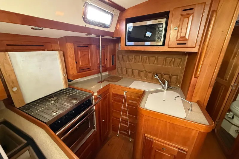 Slide: The Image of 2011 Tartan 4700 yacht kitchen with wood cabinetry, stove, microwave, and dual sinks. - 49