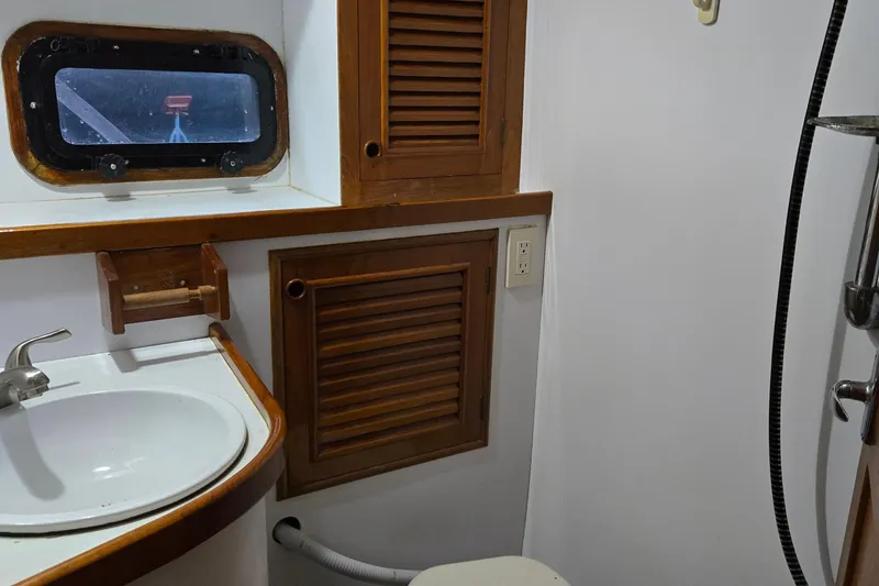 Slide: The Image of 1981 Cheoy Lee 43 Pilot House bathroom with sink, wooden cabinets, and porthole window. - 19