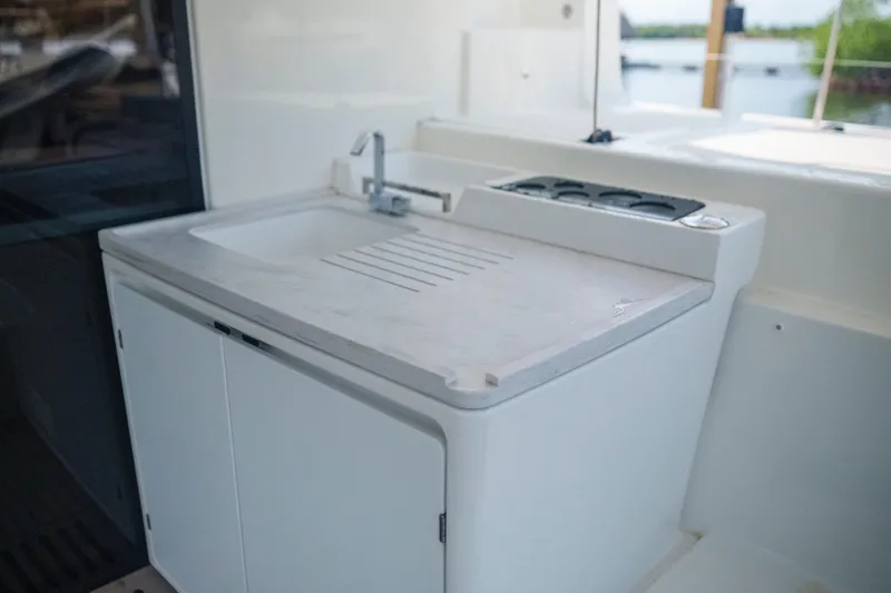 Slide: The Image of 2024 Lagoon 51 yacht kitchenette with sink and stove, featuring sleek white cabinetry. - 26