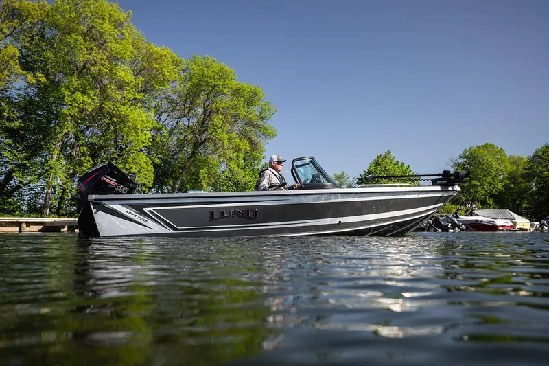 Slide: The Image of Manufacturer Provided Image: 2025 Lund 1975 Tyee boat on a serene lake with lush green trees. - 29