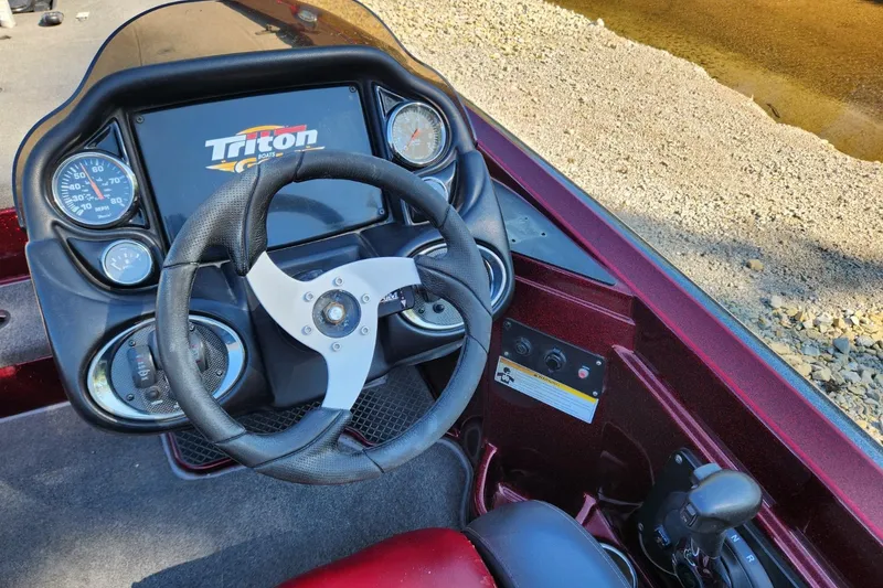 Slide: The Image of 2013 Triton 19XS boat dashboard with steering wheel and gauges near a shoreline. - 16