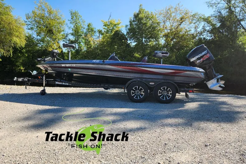 Slide: The Image of 2013 Triton 19XS boat with Mercury engine, parked on gravel, surrounded by trees. - 2