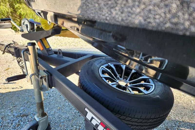 Slide: The Image of Trailer with spare tire for 2013 Triton 19XS boat on gravel surface. - 22