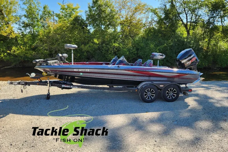 Slide: The Image of 2013 Triton 19XS boat on trailer, parked near trees, with Tackle Shack logo. - 3