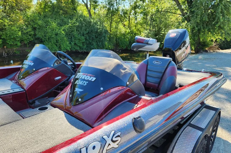 Slide: The Image of 2013 Triton 19XS boat with dual consoles, parked near a lush, green riverside. - 9