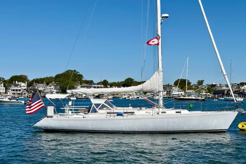 The Image of Sailboat J/47 from 1991 on calm waters, with American flag, coastal town backdrop. - 0