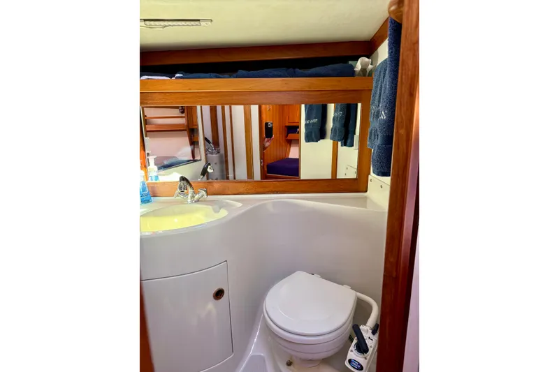 Slide: The Image of 1991 J/Boats yacht bathroom with sink, mirror, and toilet, featuring wooden accents. - 16