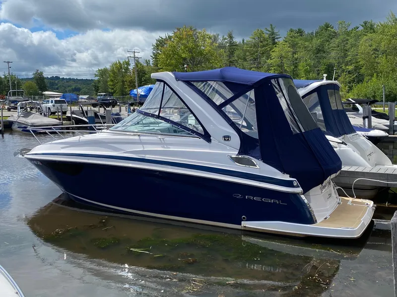 Slide: The Image of 2019 Regal 28 Express boat docked on a calm lake with lush green surroundings. - 10