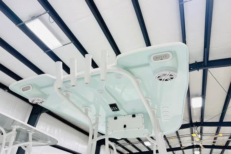 Slide: The Image of 2026 BlackJack blackjack 224 boat T-top with rod holders and speakers in a warehouse. - 6