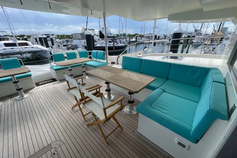 Slide: The Image of Luxurious 2018 Serenity 64 yacht deck with turquoise seating and wooden tables at marina. - 17