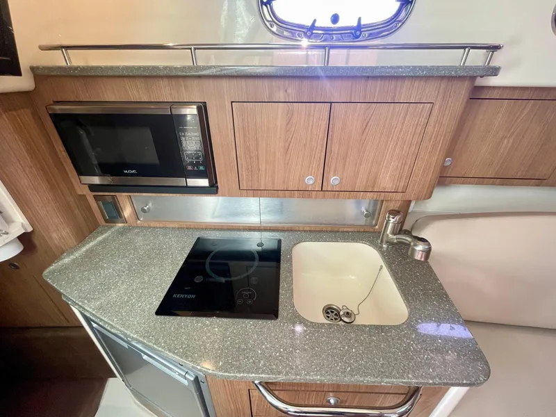Slide: The Image of 2018 Boston Whaler 315 Conquest kitchen with microwave, stove, sink, and wooden cabinetry. - 34