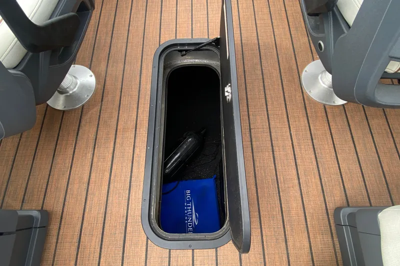 Slide: The Image of 2024 Manitou 22 MAX Explore Navigator Stealth boat storage compartment with teak flooring. - 22