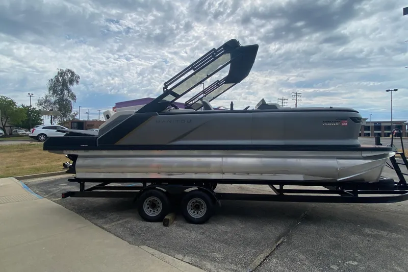 Slide: The Image of 2024 Manitou 22 MAX Explore Navigator Stealth pontoon boat on trailer, parked outdoors. - 7