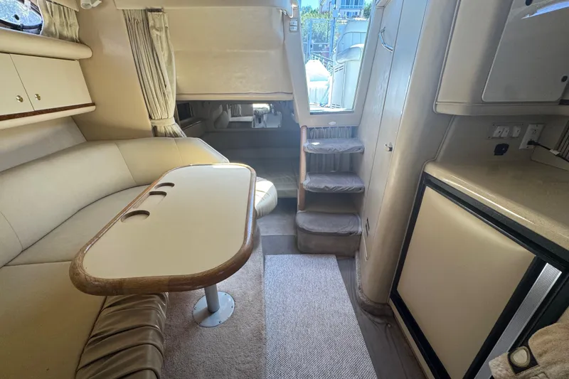 Slide: The Image of 1998 Sea Ray 330 Sundancer interior with beige seating, table, and compact kitchen area. - 15
