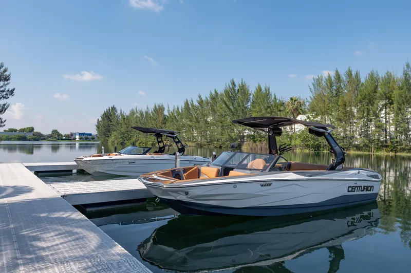 Slide: The Image of 2025 Centurion Nv233 boats docked on a serene lake under a clear blue sky. - 20