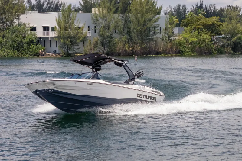 Slide: The Image of 2025 Centurion Nv233 boat cruising on a scenic lake with lush greenery. - 34