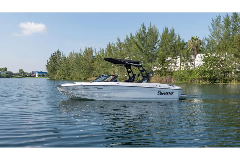 The Image of 2025 Supreme S220 boat cruising on a serene lake with lush greenery in the background. - 0