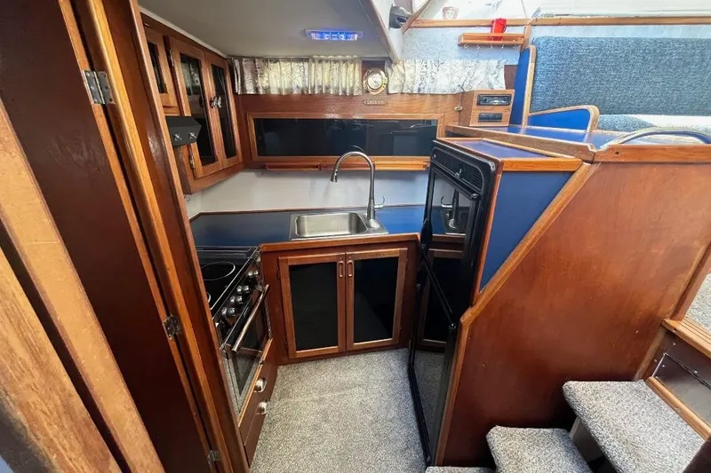 Slide: The Image of 1973 Uniflite Sport Fisher interior with wooden cabinetry, compact kitchen, and carpeted stairs. - 79