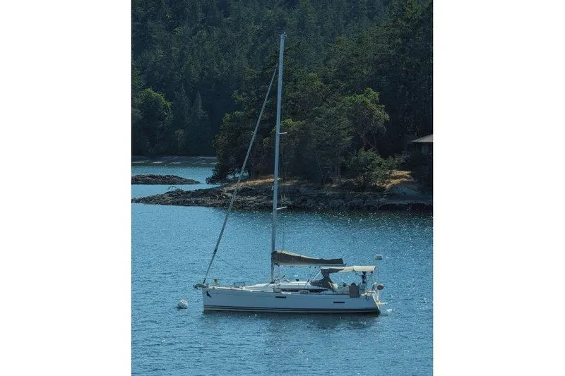 Slide: The Image of 2013 Jeanneau 379 sailboat anchored in a serene, forested bay. - 51