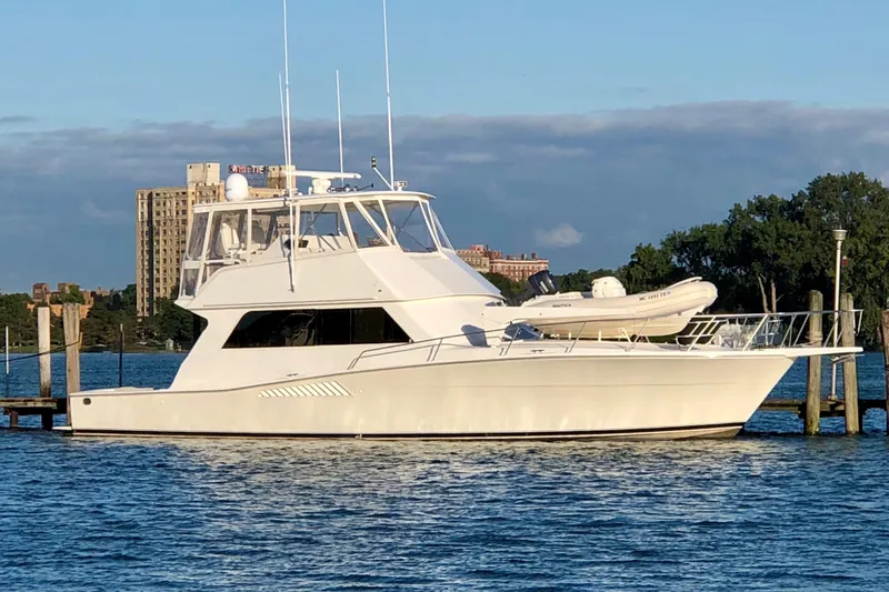 Slide: The Image of 1996 Viking 53 Convertible yacht docked on calm water with cityscape background. - 0