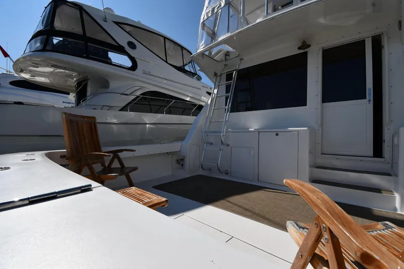 Slide: The Image of 1996 Viking 53 Convertible yacht deck with wooden chairs and ladder, docked beside another boat. - 10