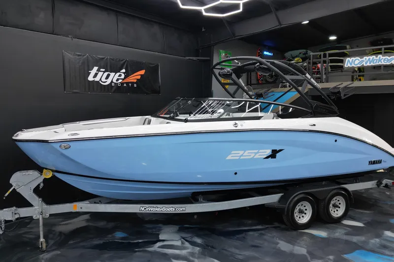 The Image of 2024 Yamaha Boats 252XE in showroom, blue and white design on trailer. - 1
