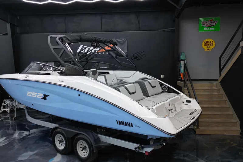 Slide: The Image of 2024 Yamaha Boats 252XE in showroom, sleek design, blue and white color, on trailer. - 4