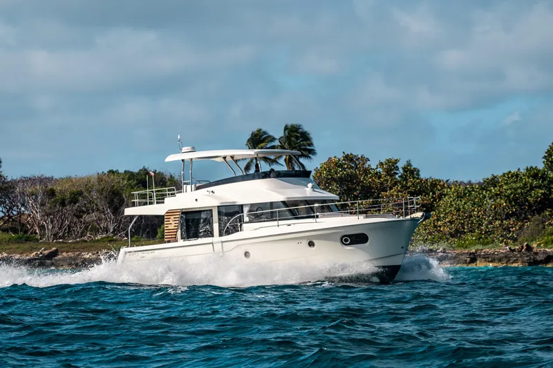The Image of 2026 Beneteau Swift Trawler 48 cruising on ocean near lush coastline. - 0